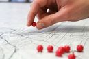 Hand placing red push pin on a detailed map. Several other pins are nearby.