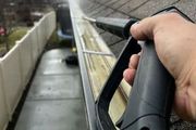 Person using a pressure washer to clean a dirty gutter on a roof.