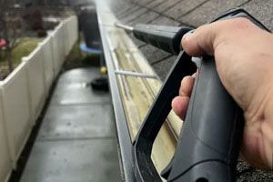Person using a pressure washer to clean a dirty gutter on a roof.