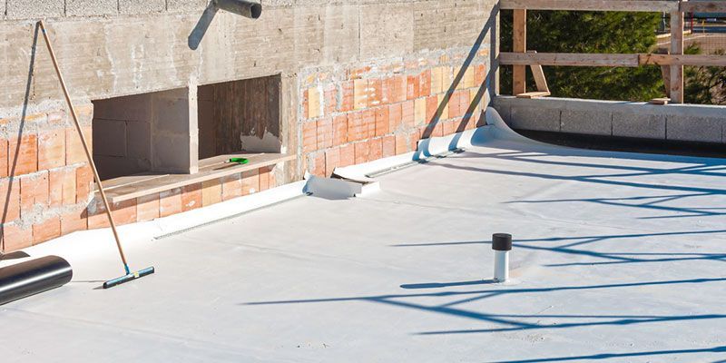 Flat roof construction with white membrane, brick wall, and tools.