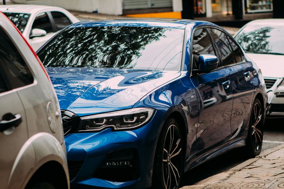Blue car parked on a city street, partially obscured by other vehicles.
