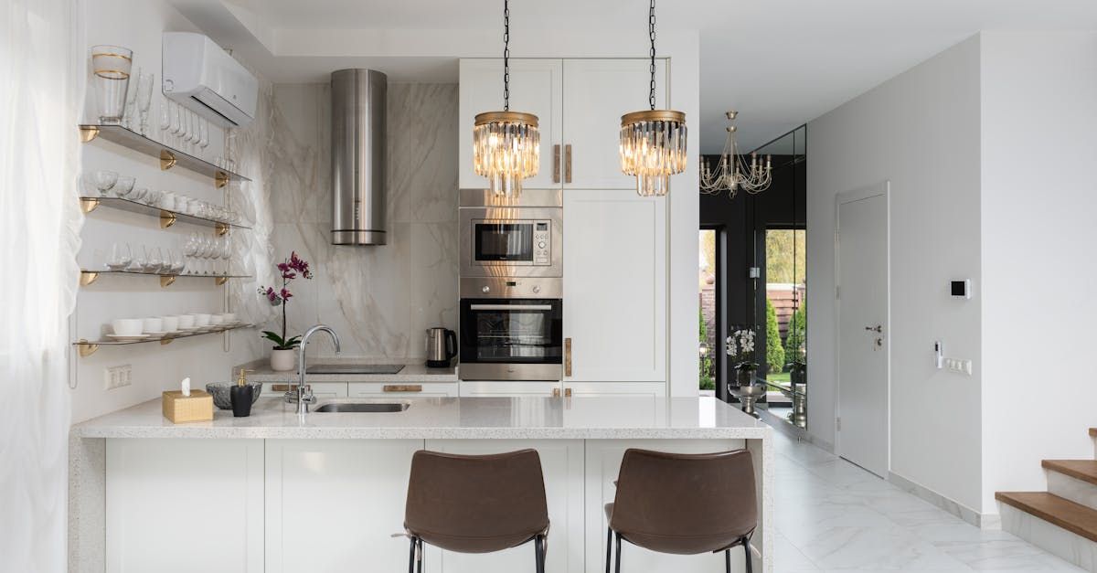 A kitchen with white cabinets , stainless steel appliances , a sink , and two stools.