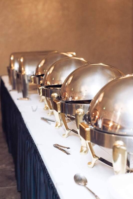 A row of stainless steel chafing dishes are lined up on a table.
