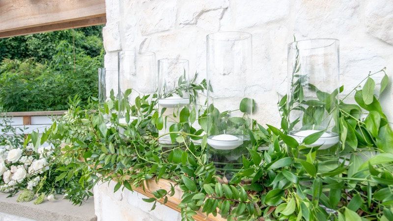 A row of vases filled with greenery and candles hanging on a wall.