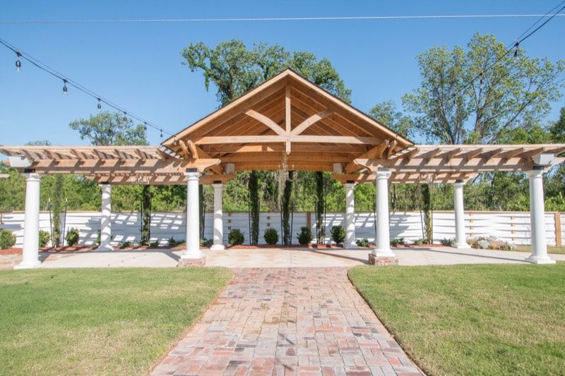 A wooden pergola with a brick walkway leading to it.