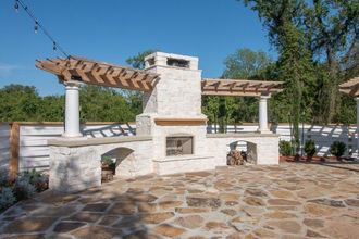 A stone patio with a fireplace and a pergola.
