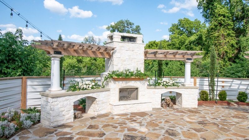 A stone patio with a fireplace and a pergola.