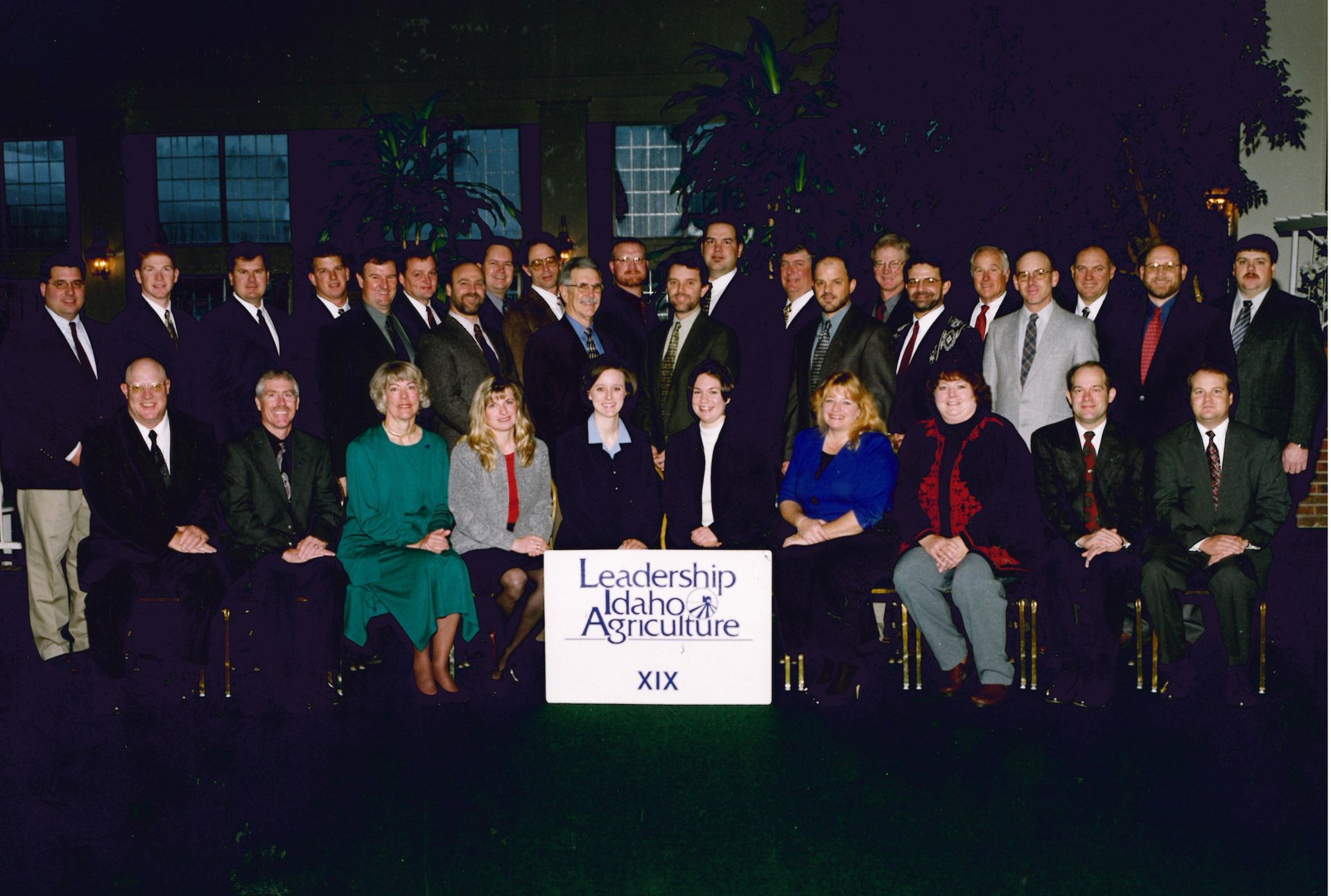 A large group of people in business attire posing for a photo behind a sign labeled