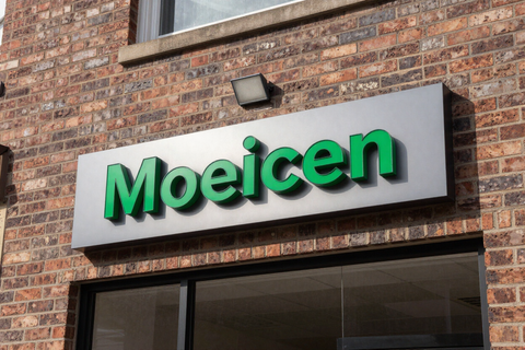 Moeicen storefront sign with green lettering on a gray panel above a brick building entrance