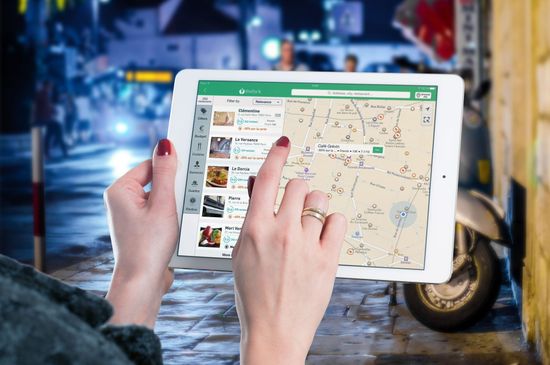 Hands using a tablet with a map app and search results outdoors at night
