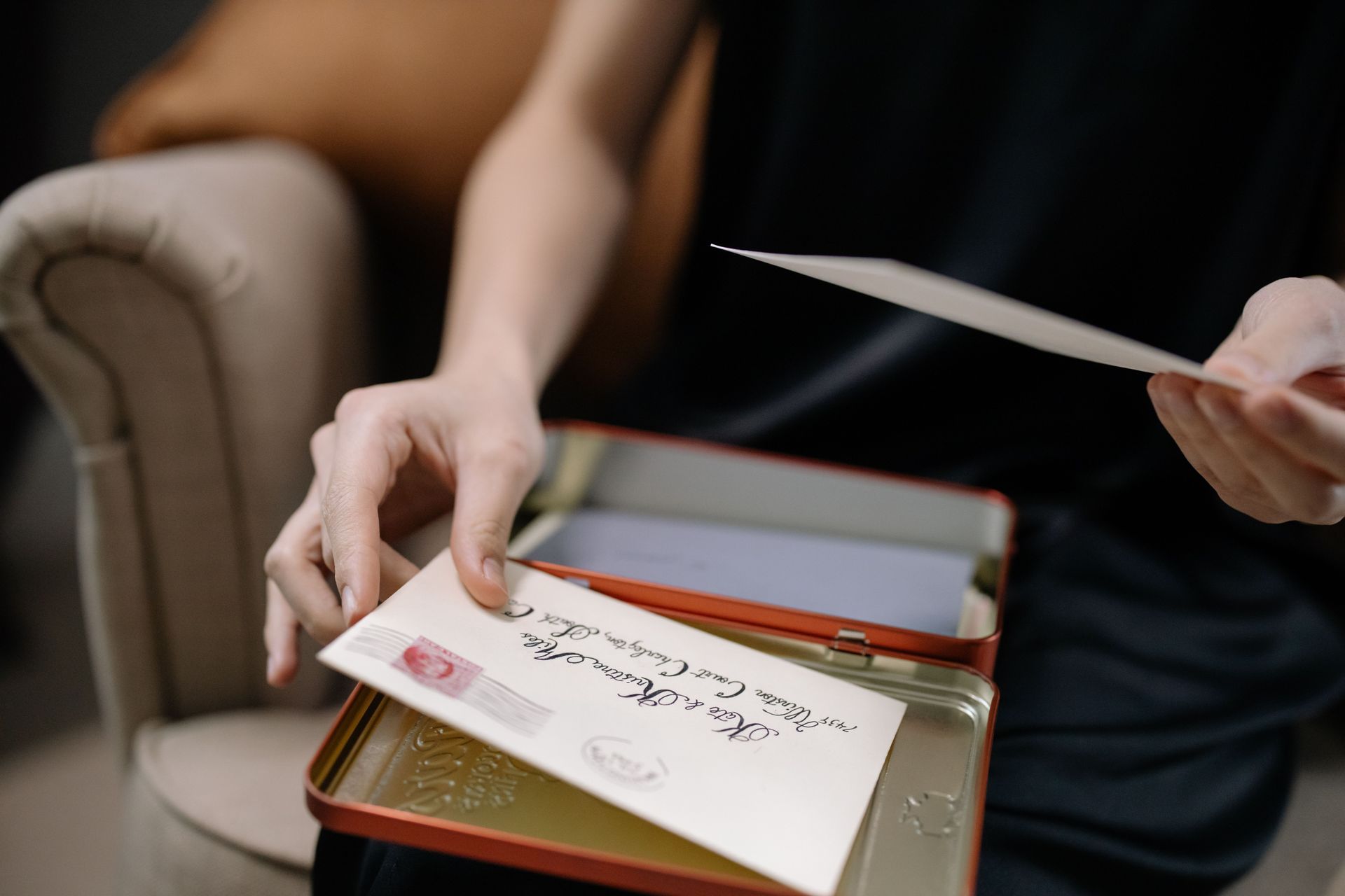 Person opening a gift box with a handwritten card and envelope on a couch