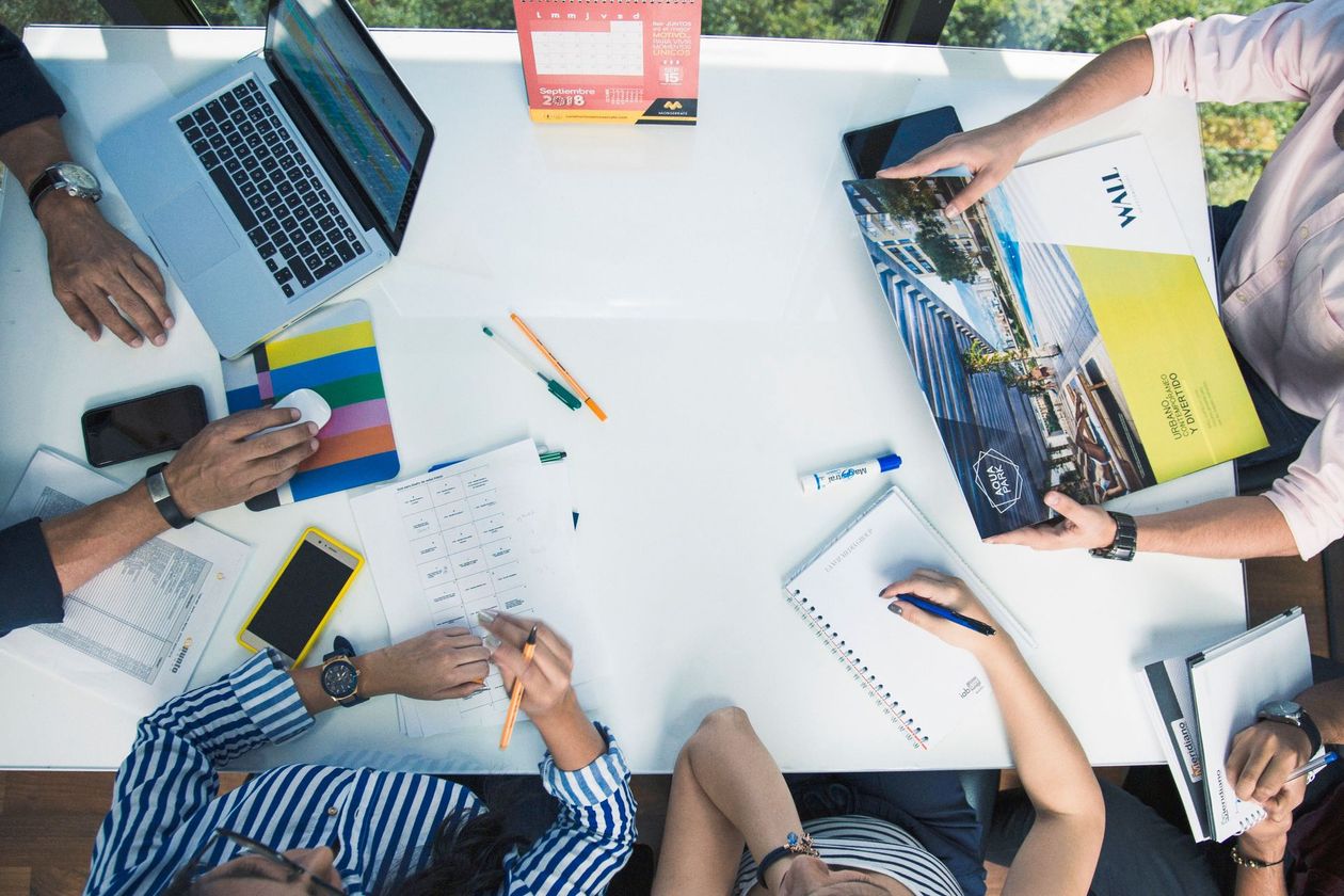 People collaborating around a white table with laptops, notebooks, and colorful charts in a meeting.