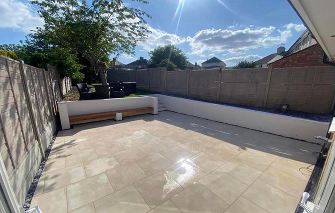 A patio with a bench and a fence in the backyard of a house.