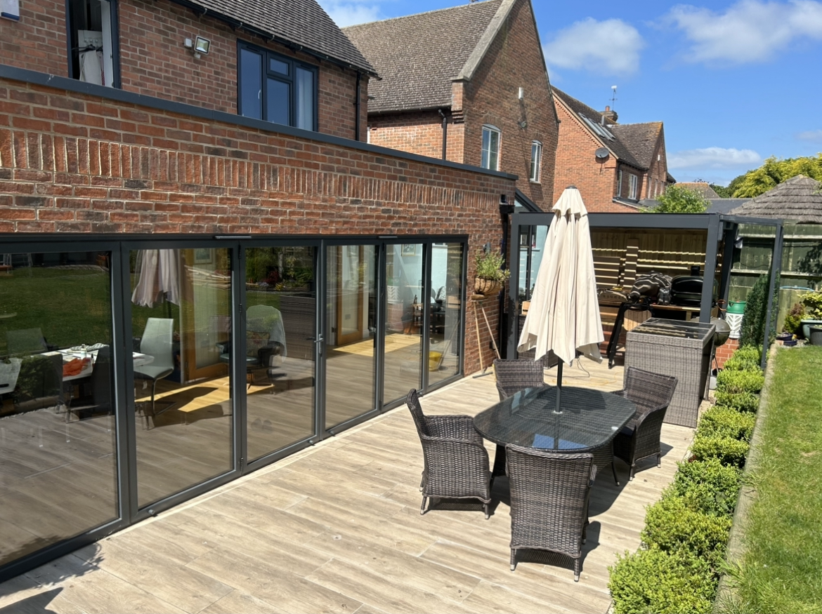 A patio with a table and chairs and an umbrella in front of a brick house.