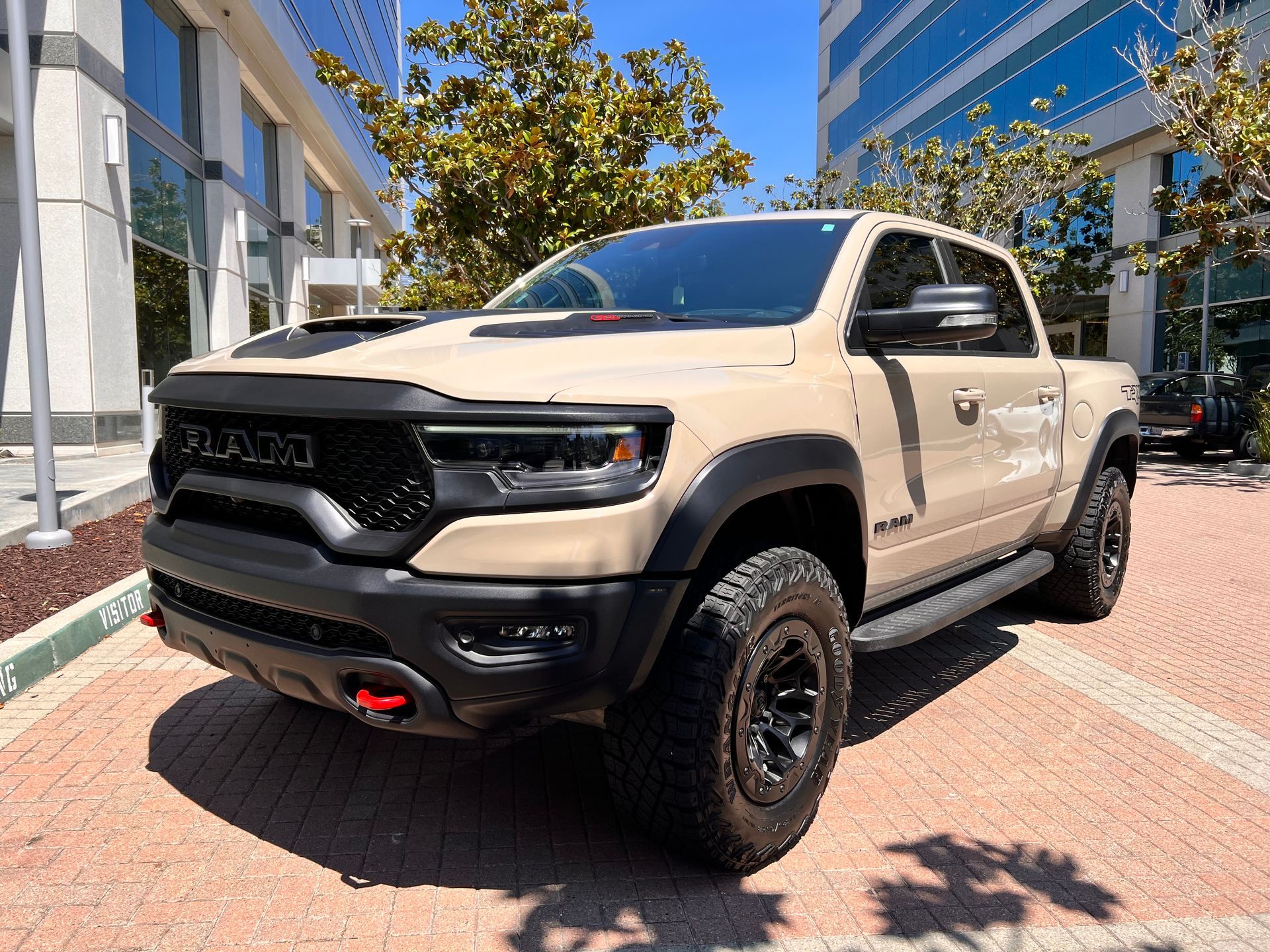A tan ram truck is parked in a parking lot in front of a building.