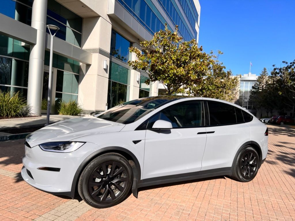A white tesla model x is parked in front of a building.