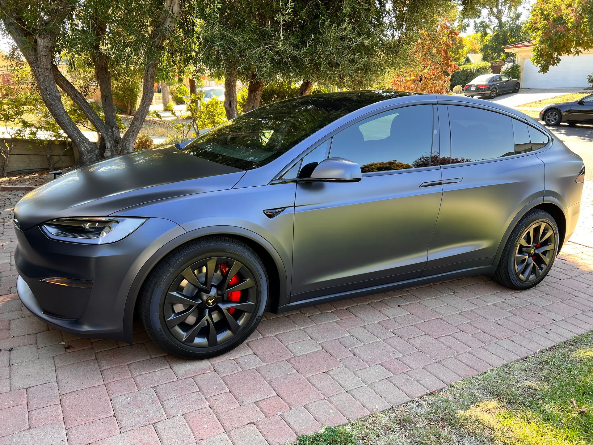 A black tesla model x is parked on a brick driveway.