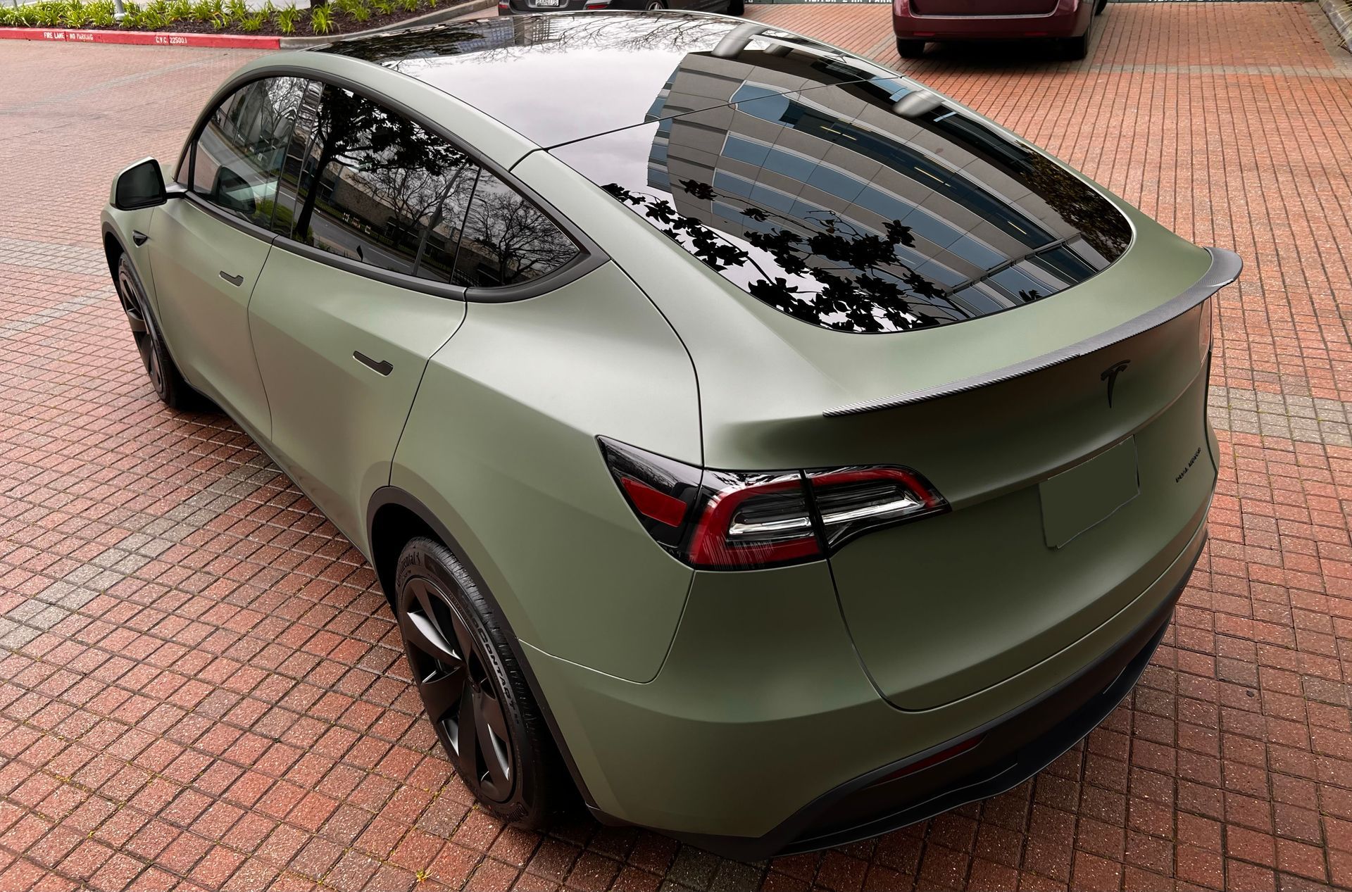A green tesla model y is parked on a brick driveway.
