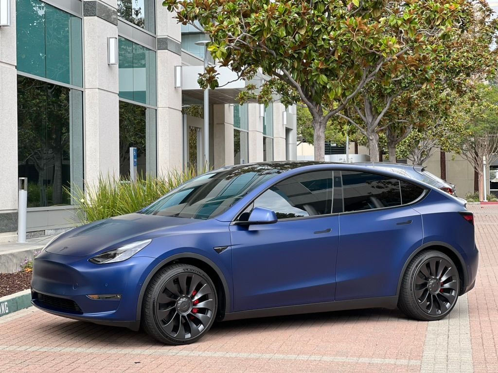 A blue tesla model y is parked in front of a building.