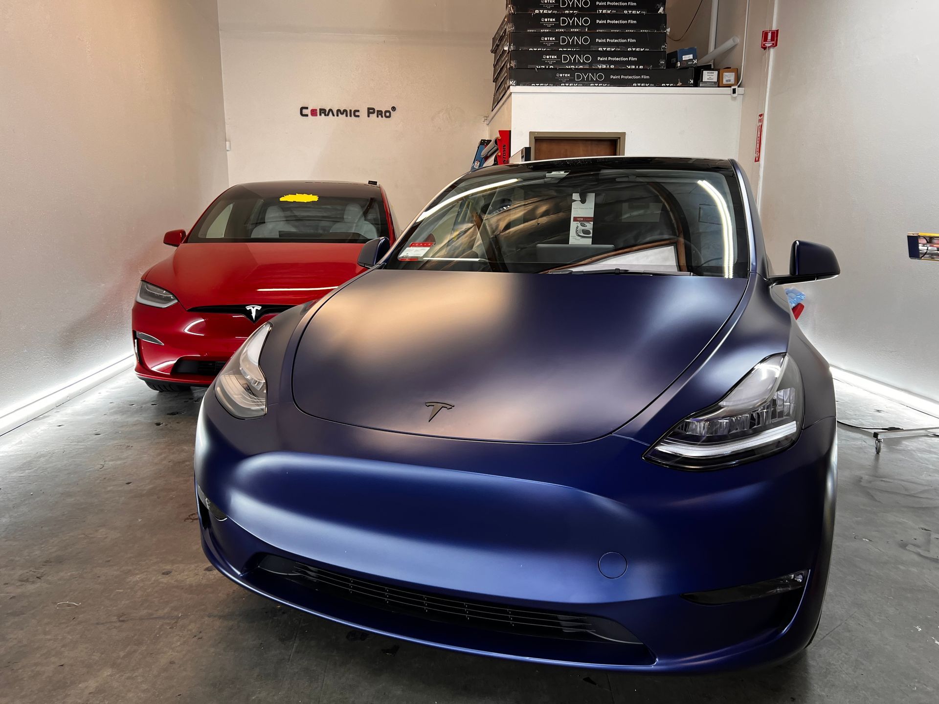 A blue tesla model 3 is parked next to a red tesla model 3 in a garage.