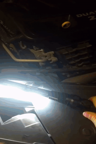 A person is holding a flashlight under the hood of a car.
