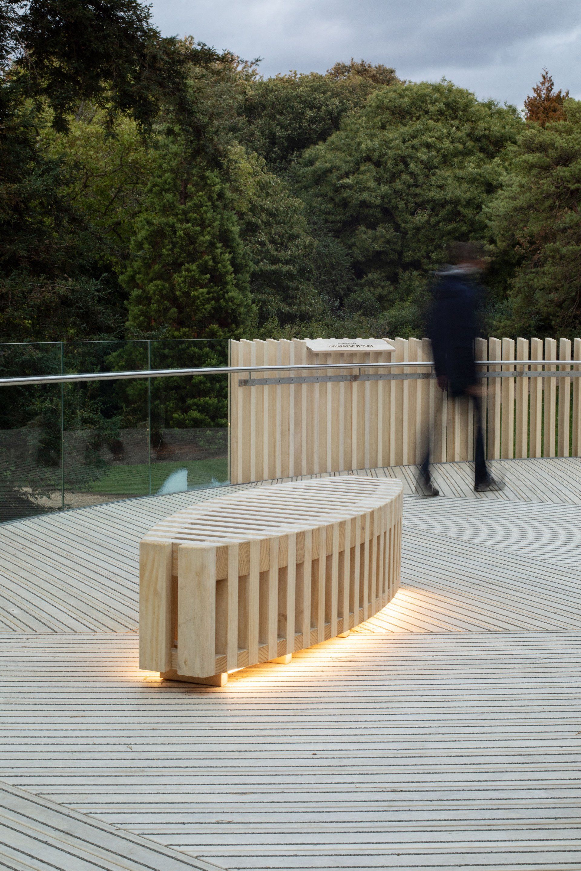 A person is walking past a wooden bench on a wooden deck.