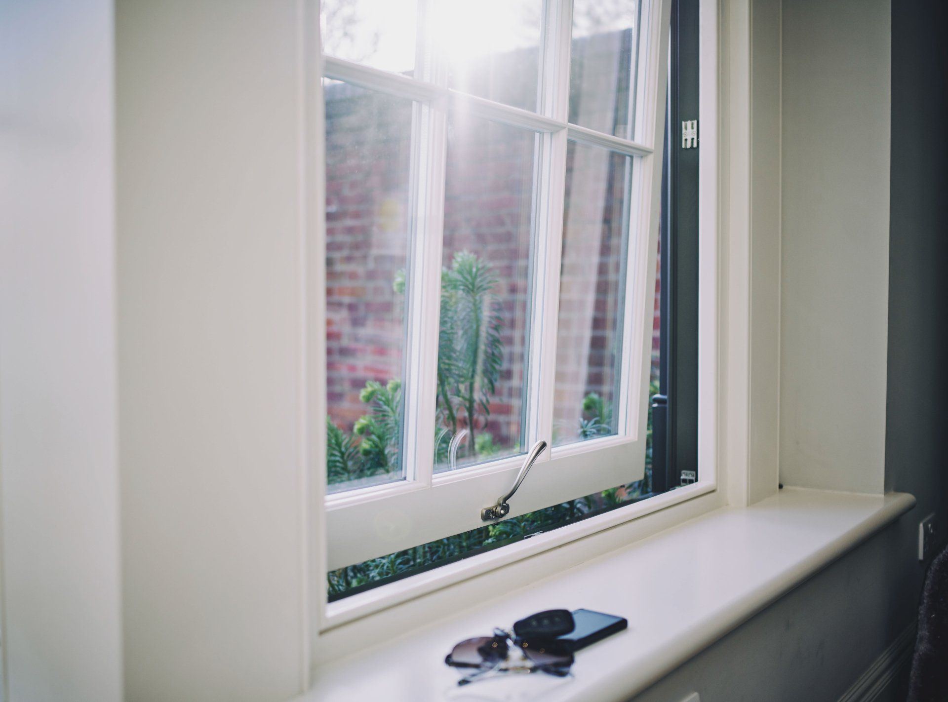 A window with a cell phone and sunglasses on the window sill.