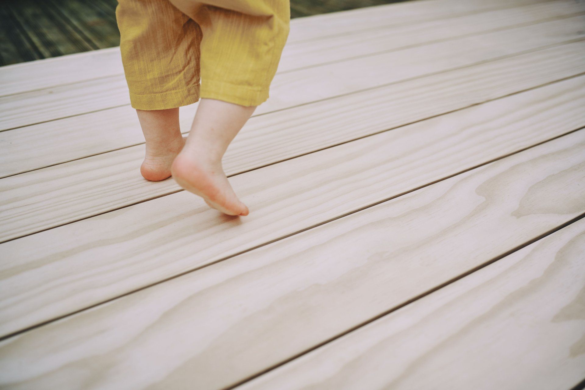 A child is walking barefoot on a wooden deck.