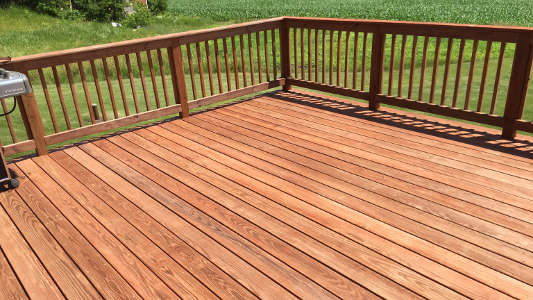 A wooden deck with a grill on it and a fence.