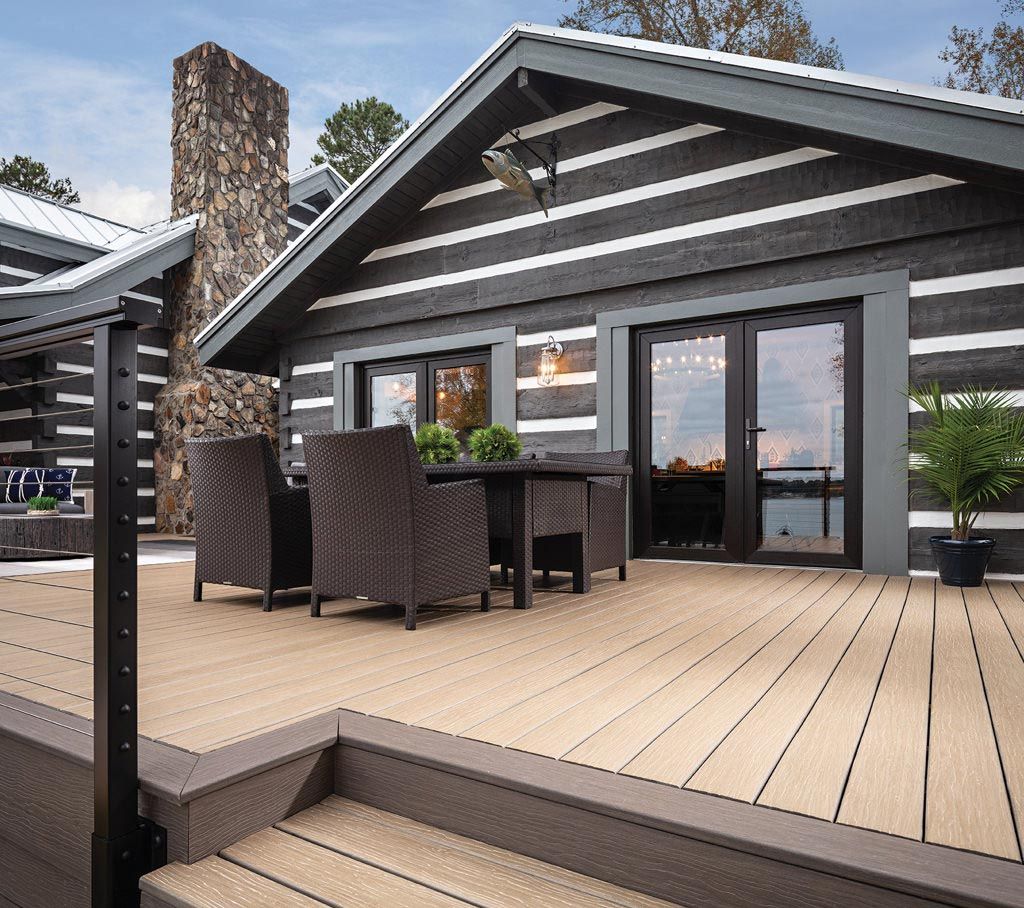 A log cabin has a large deck with a table and chairs on it.