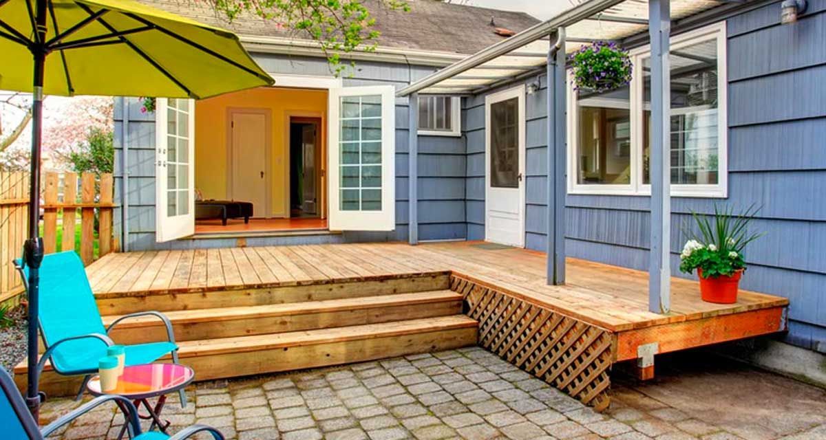A blue house with a wooden deck and umbrella in front of it.