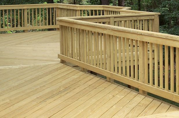 A wooden deck with a railing and trees in the background.