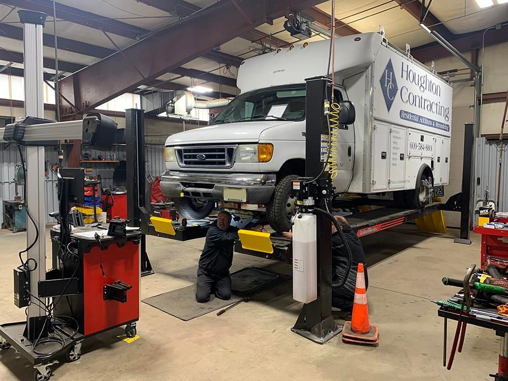 Mechanic working under a white work van lifted on a car lift in a garage. | Dave Muller Automotive & Trailer