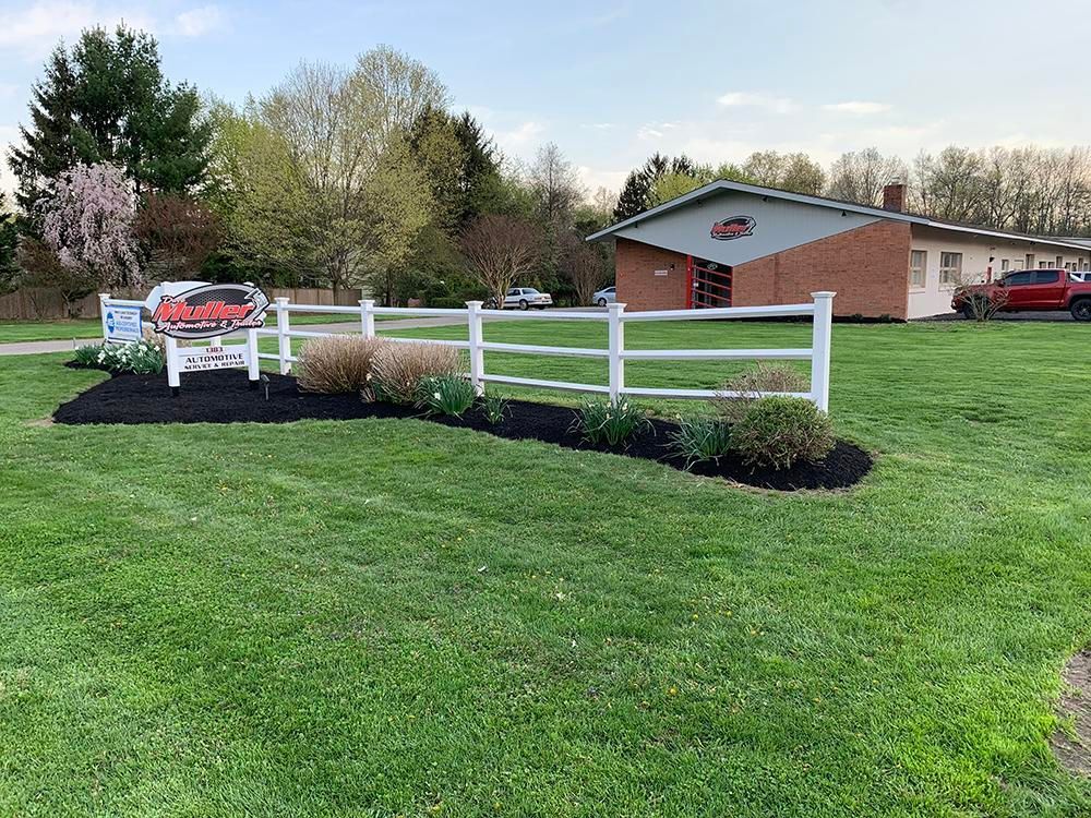White picket fence around a flower bed with a building and a red truck in the background. | Dave Muller Automotive & Trailer