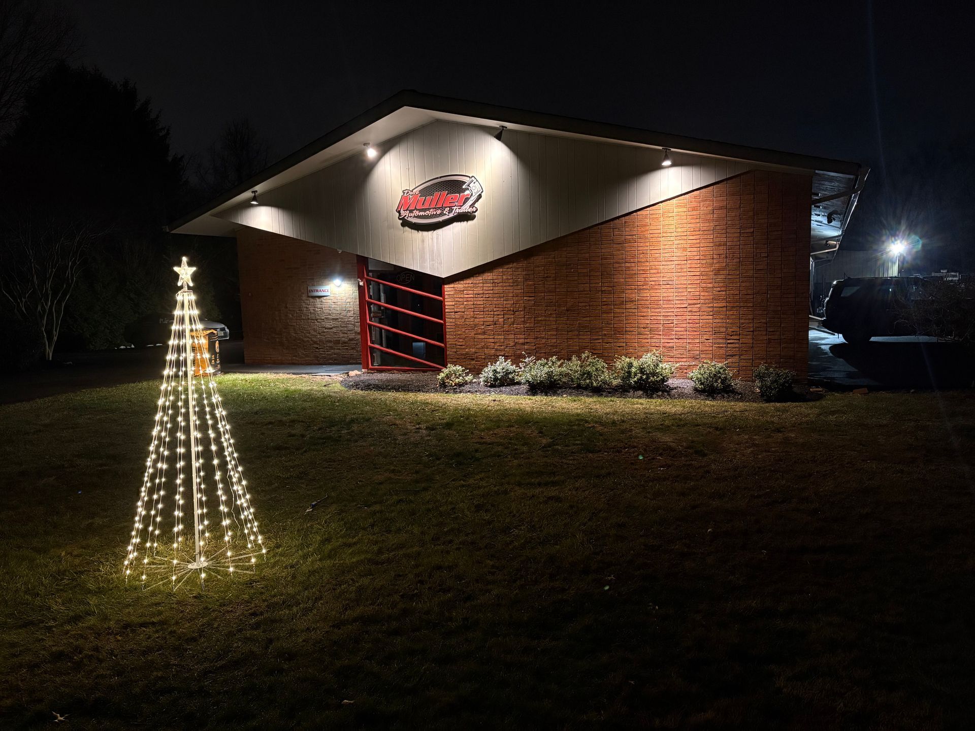A building with Christmas lights at night, featuring a lighted tree in front. | Dave Muller Automotive & Trailer