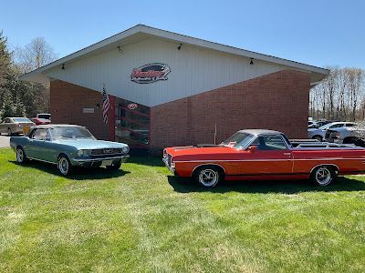 Two classic cars parked in front of a brick building on a sunny day. | Dave Muller Automotive & Trailer