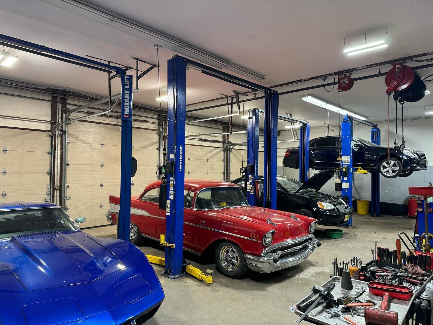 Car repair shop: classic red car, blue Corvette, multiple cars on lifts. Tools visible. | Dave Muller Automotive & Trailer
