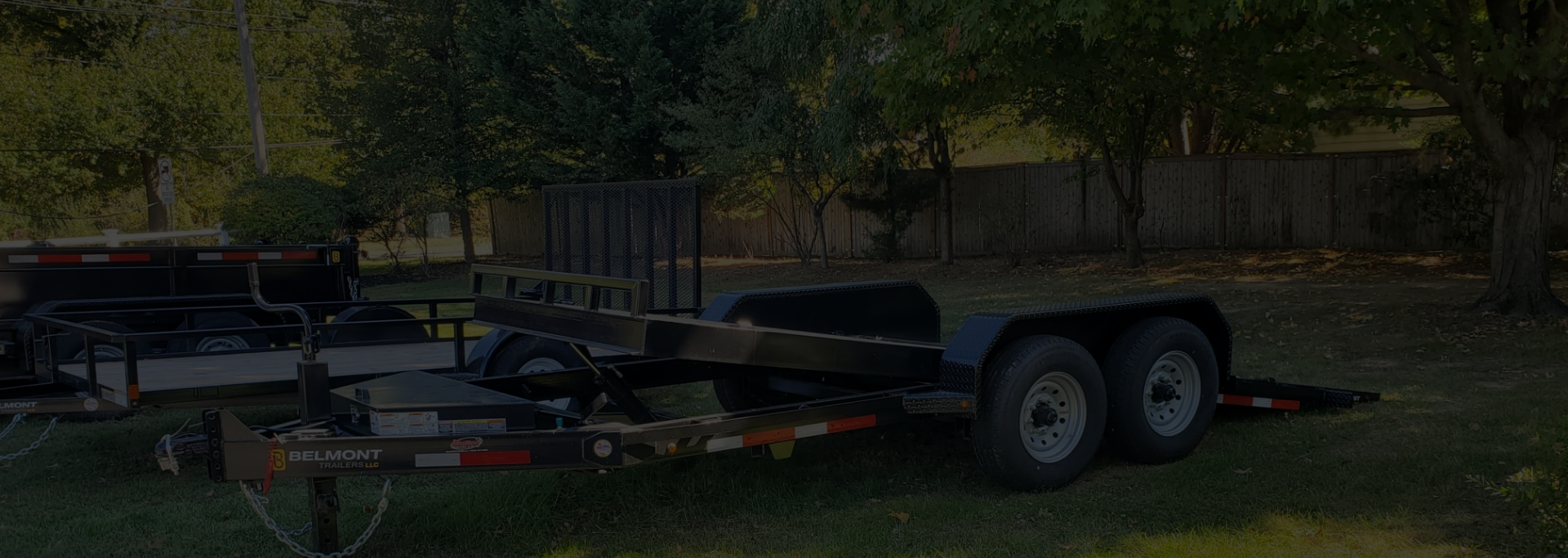 Two black trailers parked on grass with trees and a fence in the background. | Dave Muller Automotive & Trailer