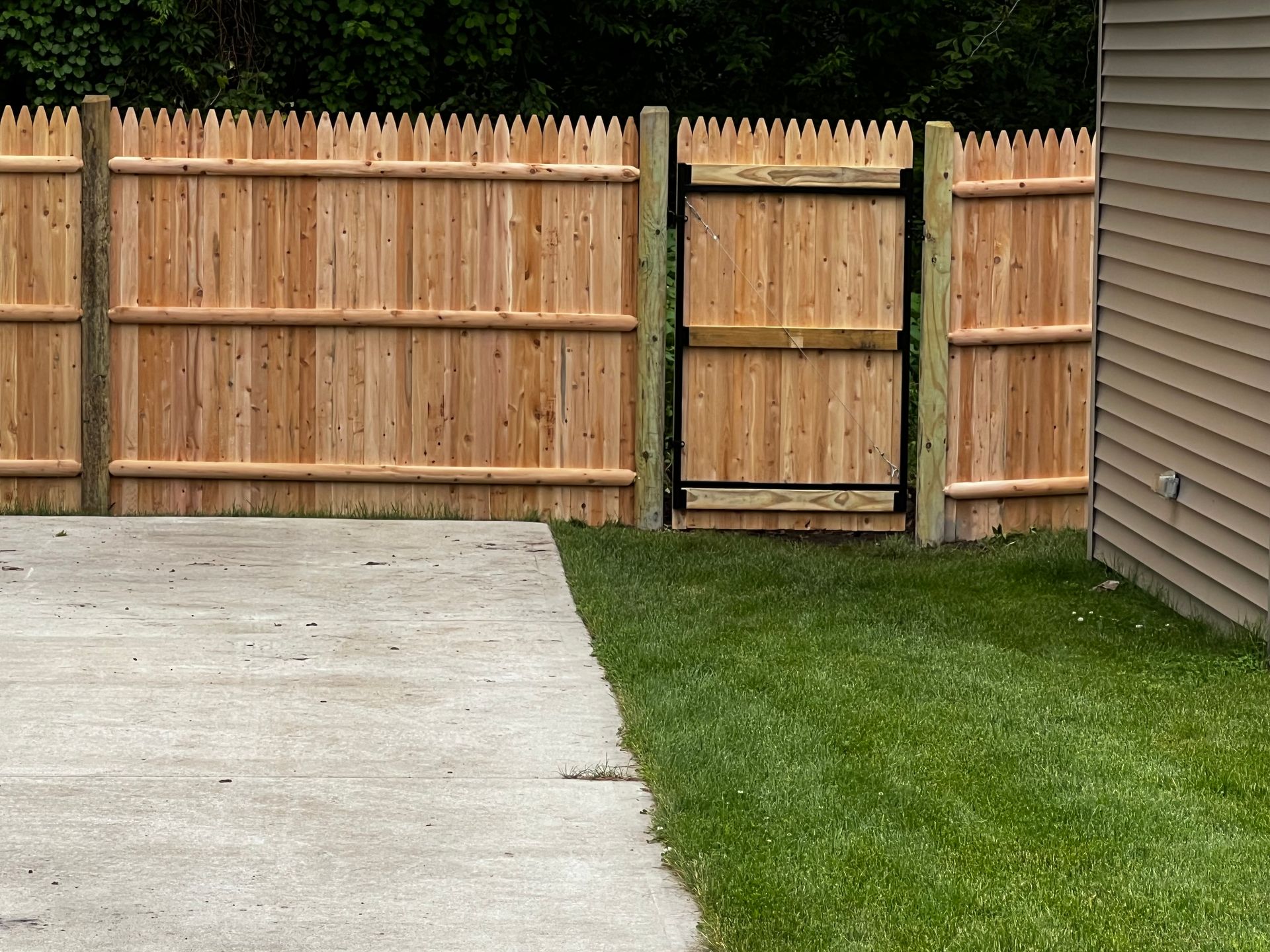 Wooden fence with gate next to a concrete patio and a grassy lawn.