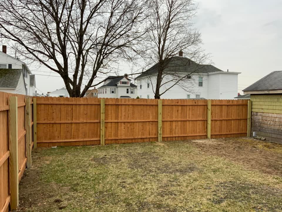Wooden privacy fence in a backyard; bare trees, houses in background.