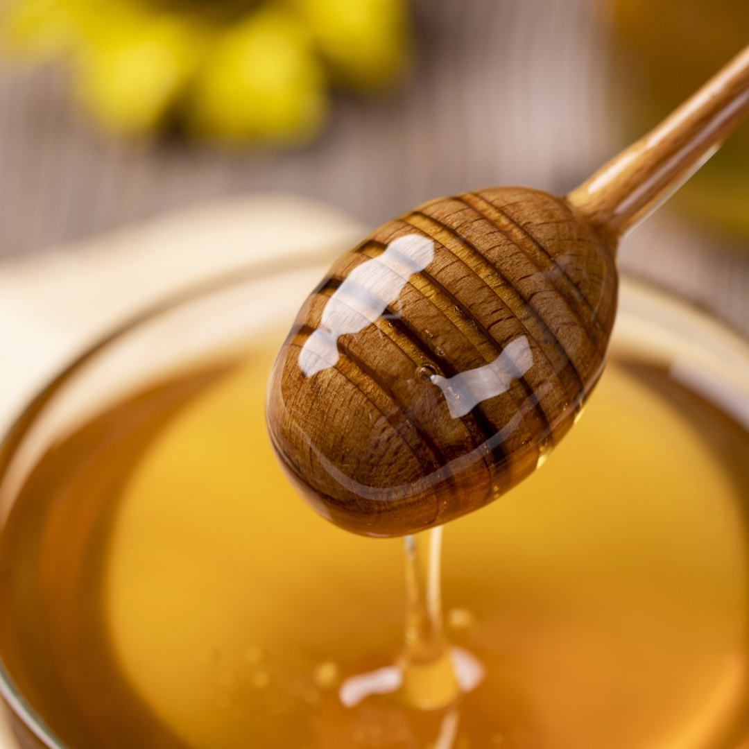 Delicious dripping honey on a honey dipper above a vat of fresh Lake Highlands Honey