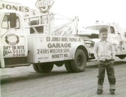A young boy smiles next to a tow truck with