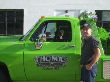 Man and dog in a green tow truck. 