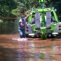 Man in water near green tow truck.