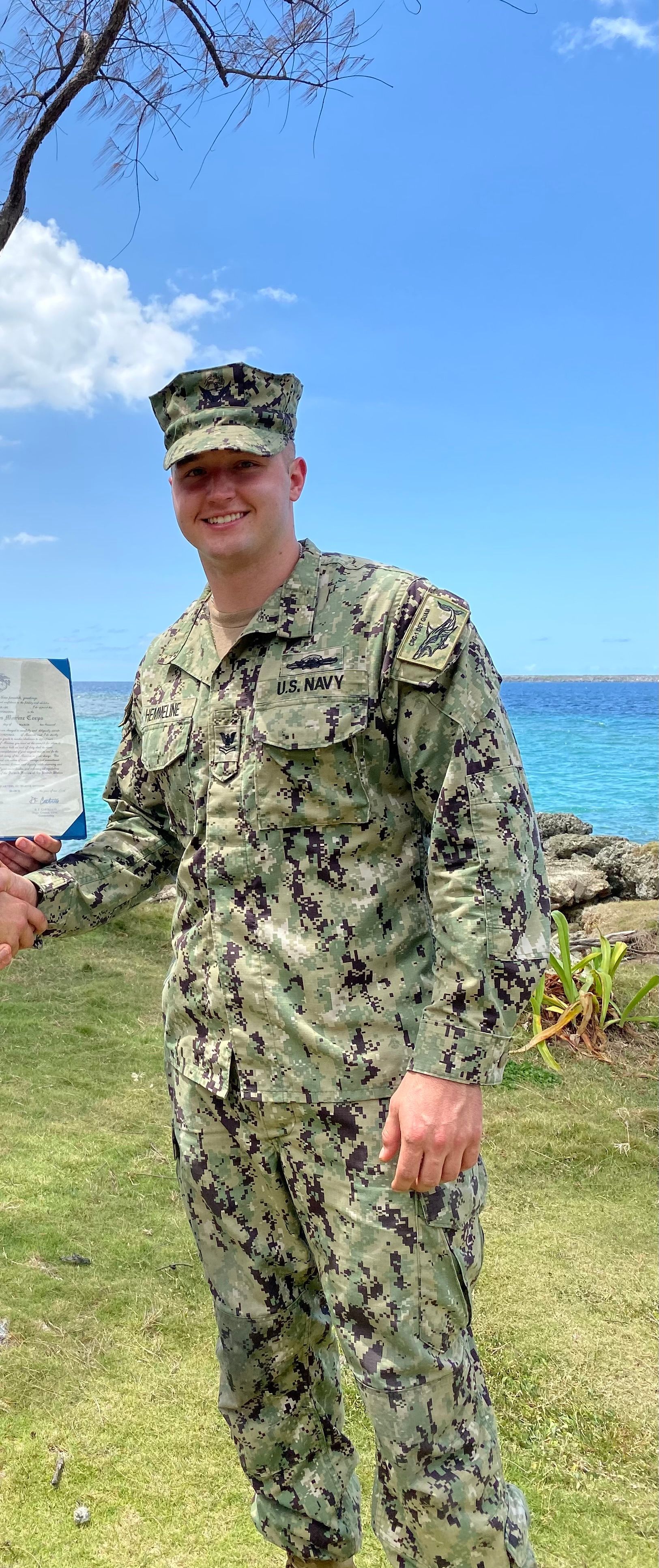 A man in a military uniform is holding a plaque in front of the ocean.