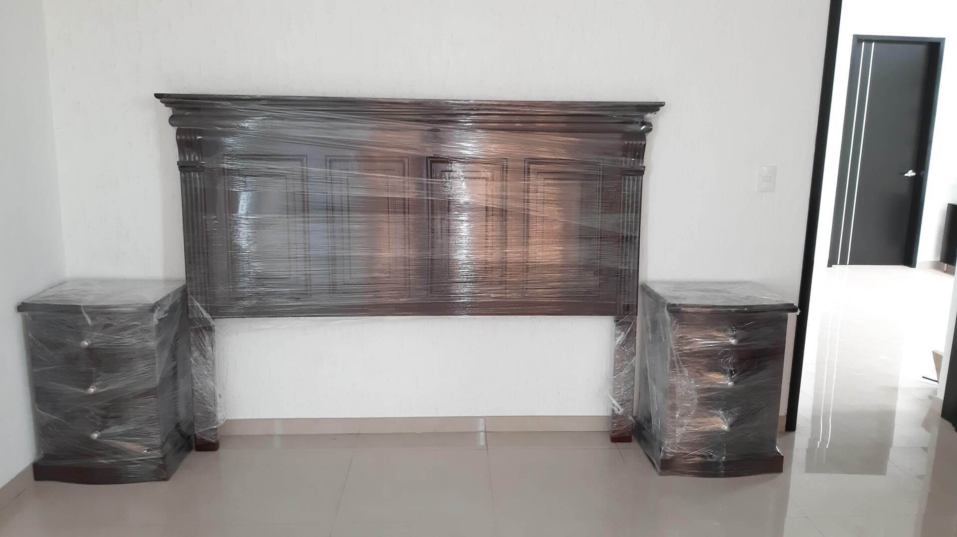 Un dormitorio con cabecero y dos mesitas de noche envueltas en plástico.