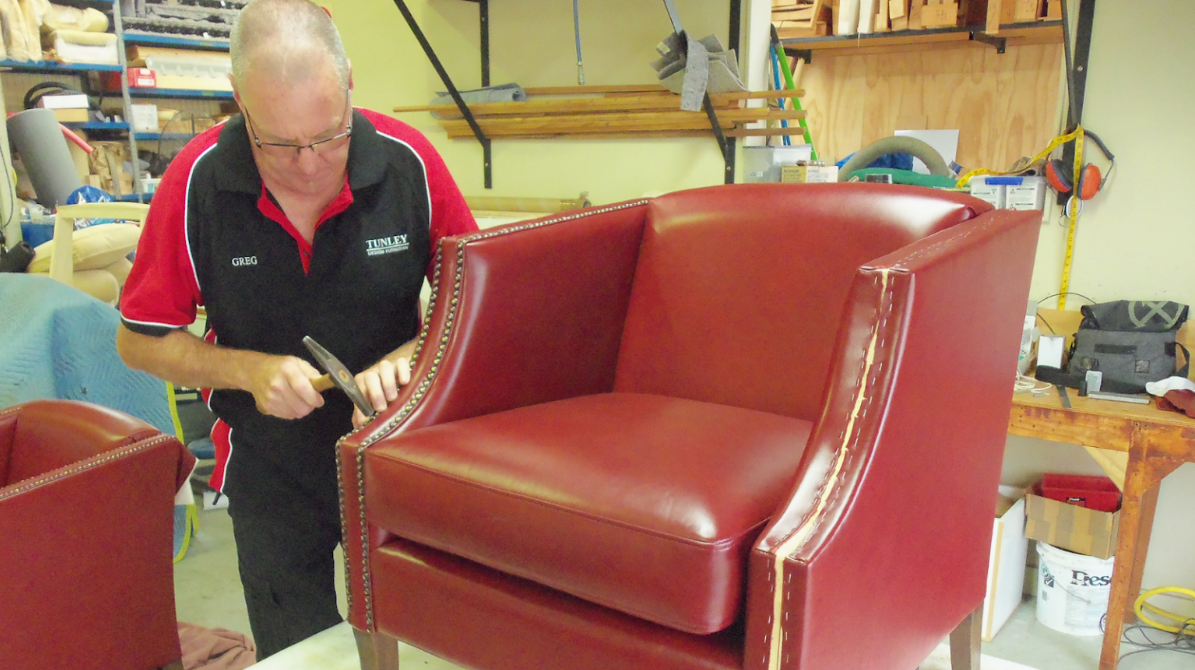 A man is working on a red leather chair in a workshop.