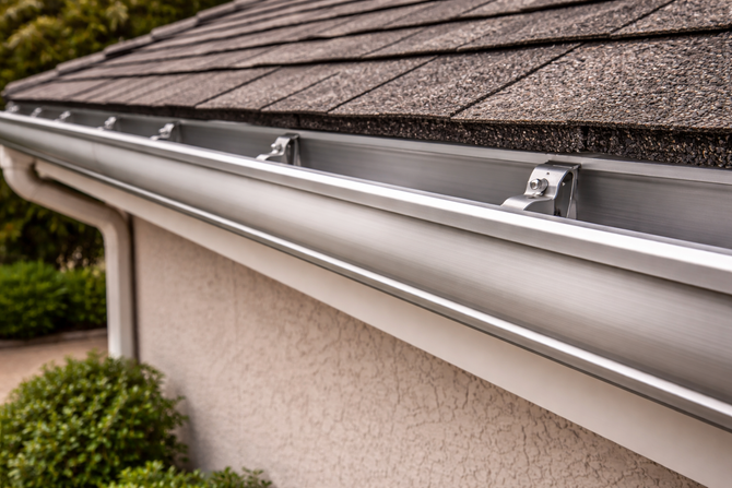 Rain gutter along a shingled roof edge on a beige house