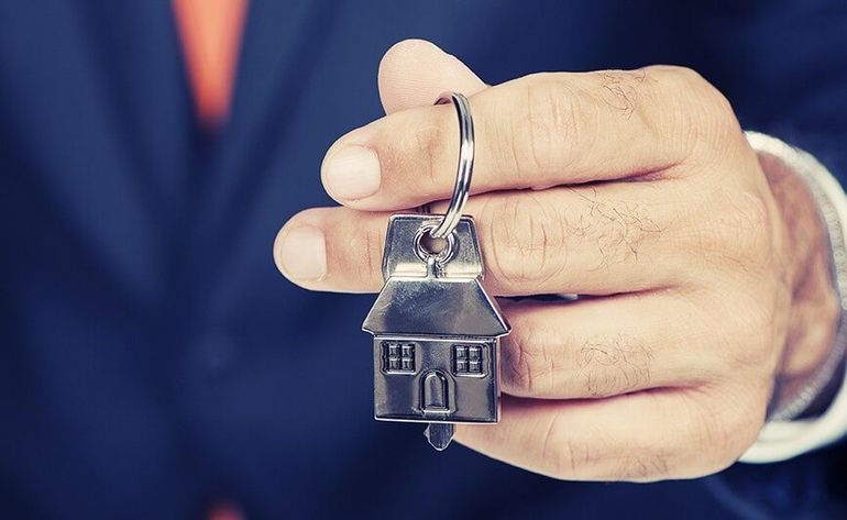 A Man Holding a Key With a House Keychain Attached to It — Licensed Conveyancing Agent in Fannie Bay, NT