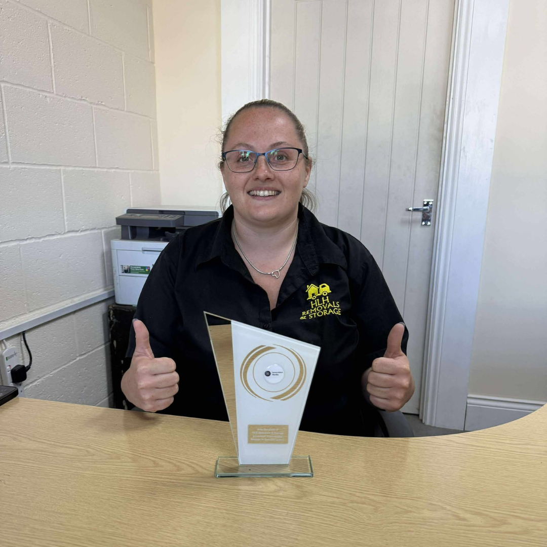 Person smiling and giving thumbs up behind a trophy on a table in a bright room